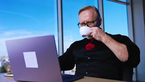 calm confident bearded man works on laptop and drinks coffee. portrait of a hard-working entrepreneur in office.