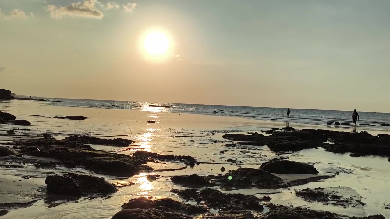 Folk går på stenstrand ved solnedgang.