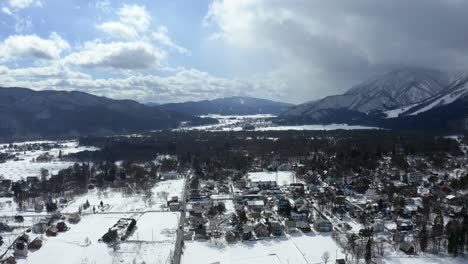 Through-aerial-cinematography,-the-drone-unveils-the-stunning-vista-of-Hakuba-valley,-where-the-winter-sun-bathes-the-landscape-in-a-radiant-glow-and-displaying-massive-clouds-attach-to-the-mountains