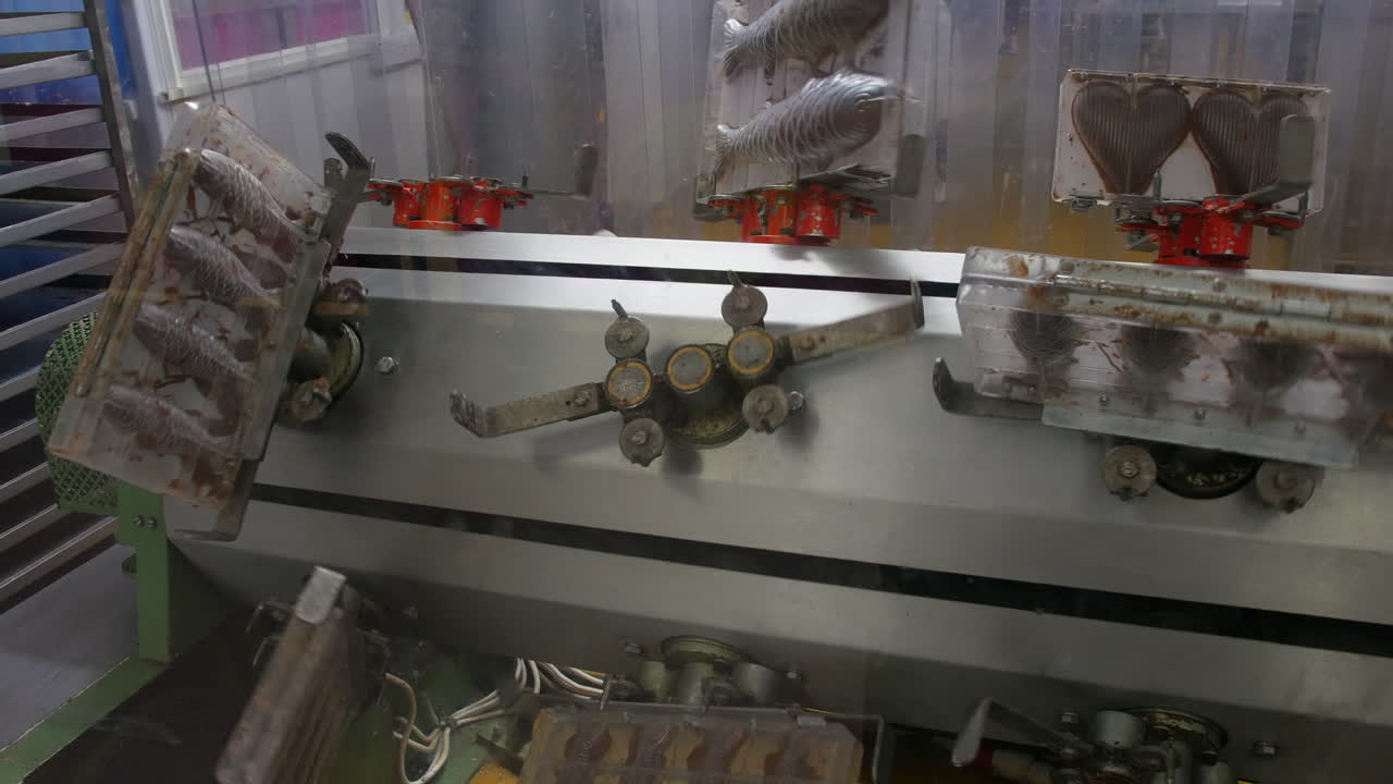 Rotating molds filled with chocolate fish shapes move through a molding machine in a sweet factory. The system evenly coats and sets the chocolate before cooling and packaging
