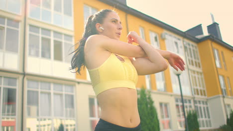 a young woman with headphones is stretching on the grass in a city park in slow motion. listen to music while playing sports