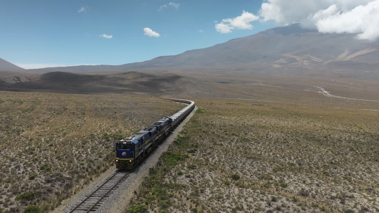 Drone frontal view of a freight train transporting multiple mineral wagons across the Peruvian Andes.