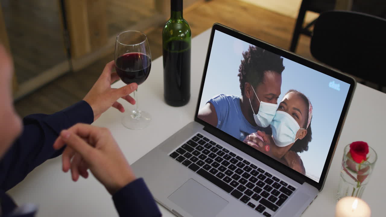 Mid section of african american woman holding wine glass while having a video call on laptop at home