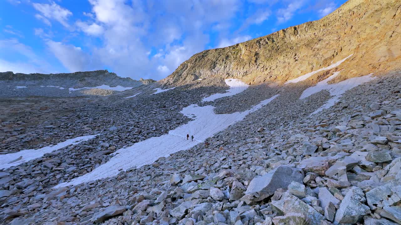 Hikers walking snow glacier melt Capitol Peak Trailhead Ridge route Mt Daly K2 Colorado Rocky Mountain Elk Range landscape sunrise morning high alpine elevation Aspen Snowmass Wilderness pan left
