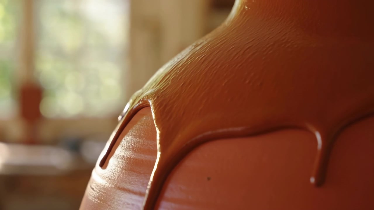 Un primo piano, leggermente angolato, di una spalla umana in un ambiente interno, probabilmente una stanza con finestre o porte a vetri sullo sfondo. La scena presenta un'atmosfera neutra ed è dominata