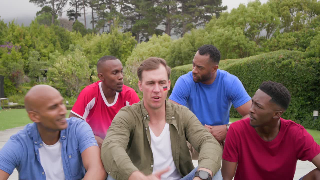 Vertical video: Diverse men laughing, leaning in park after red jersey speaking, face paint visible