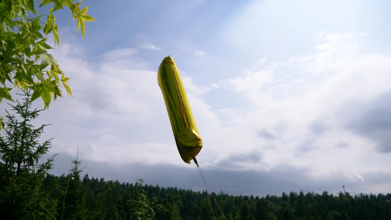 바람 속에서 슬로우 모션으로 춤을 추는 헬륨으로 채워진 최초의 팽창식 황금 풍선