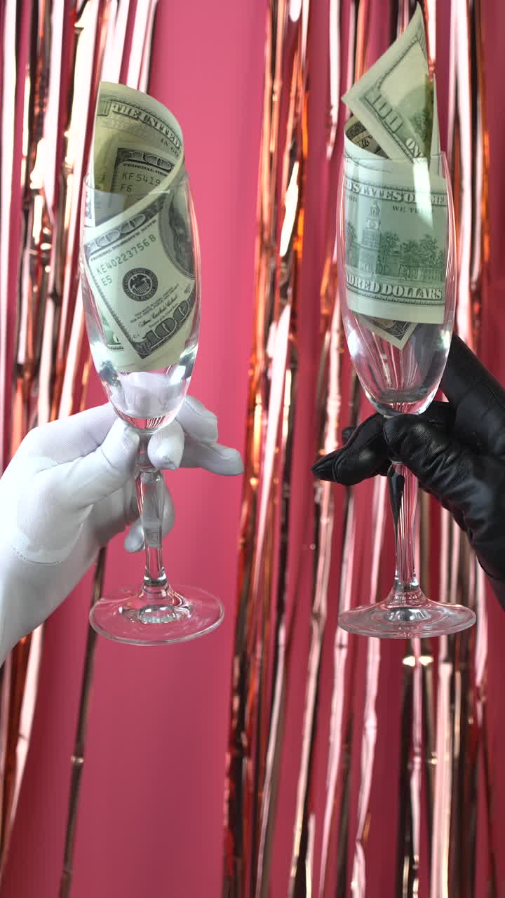 Mani con guanti che brindano con calici di champagne riempiti con banconote da cento dollari