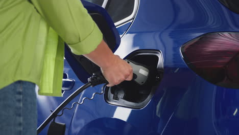 close up of woman attaching charging cable to environmentally friendly zero emission electric car