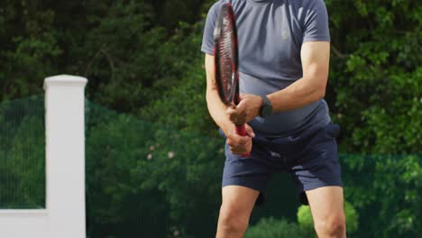 Video-of-midsection-of-focused-biracial-senior-man-playing-tennis-on-tennis-court