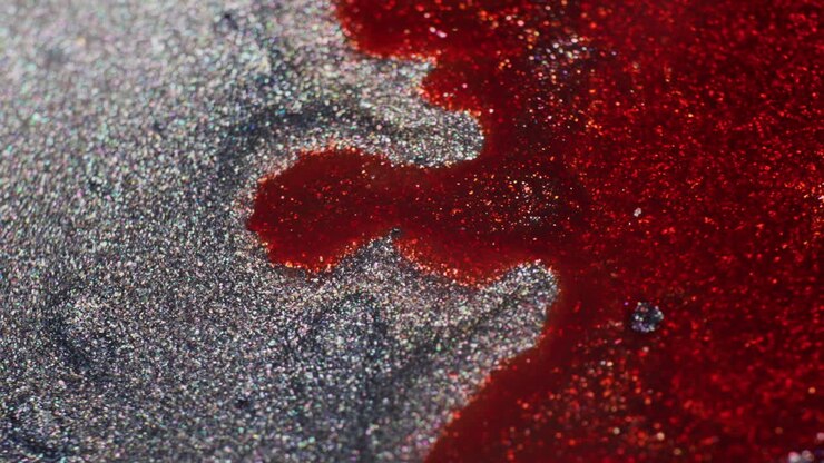 Gros plan macro d'encre gris-violet chatoyante avec de l'encre rouge ajoutée et poussée, créant un mouvement dynamique sur la surface scintillante.