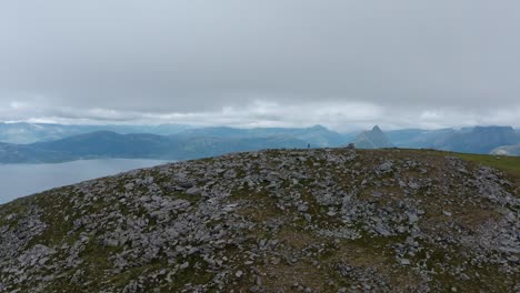 vista lejana del caminante solitario caminando en el pico de la montaña rocosa en luroy, noruega