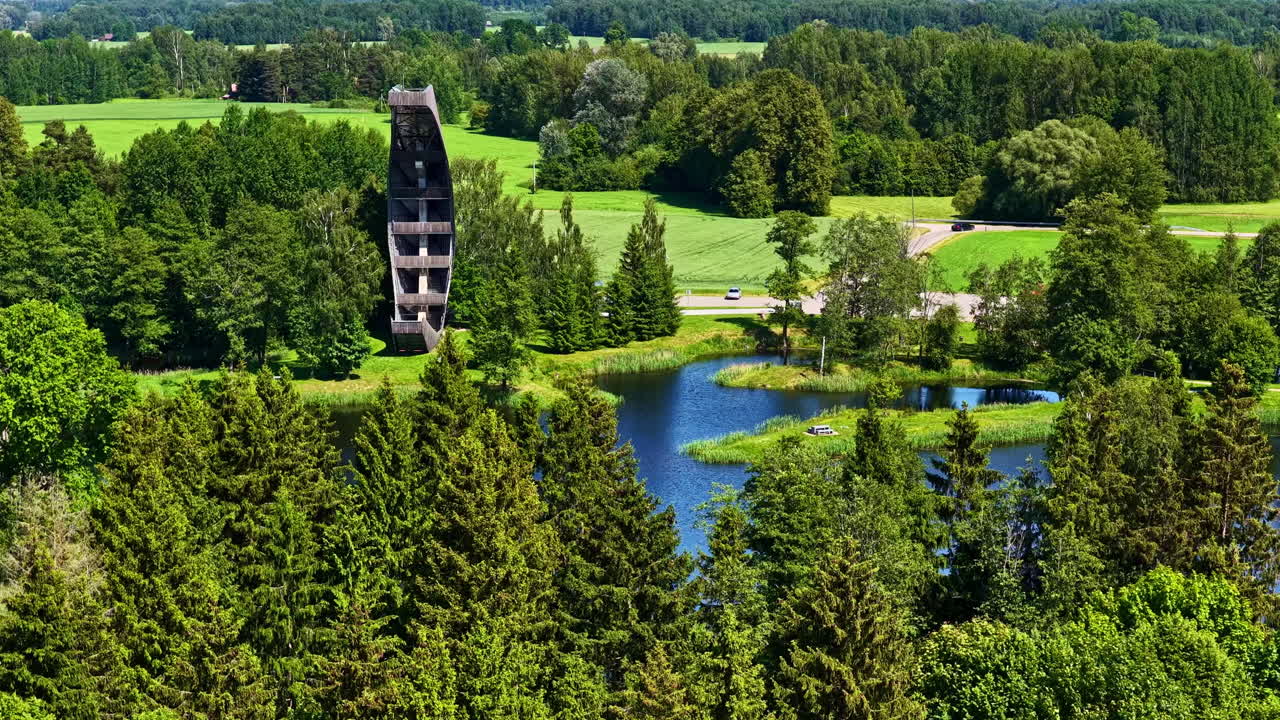 Aerial view approaching the canoe-shaped Kirkilai Observation Tower beside vivid karst lakes and lush forests in Biržai Regional Park, Lithuania