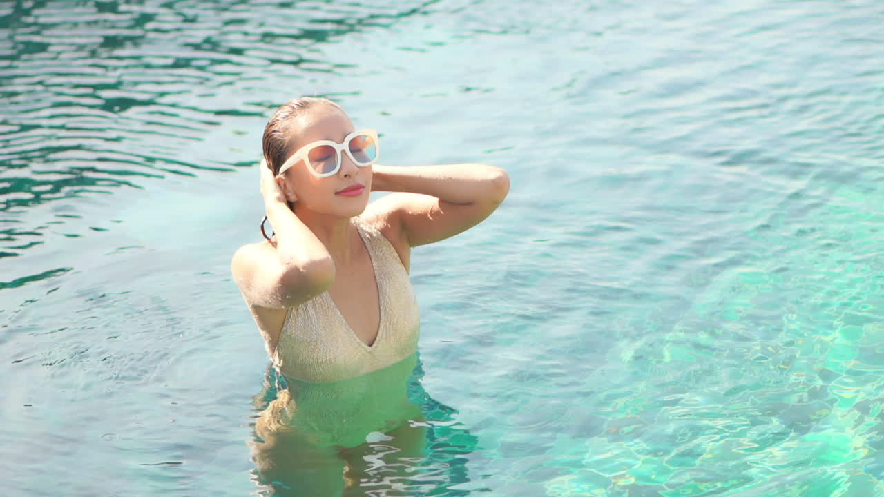 Woman standing in clear blue sea runs hands over long dark wet hair