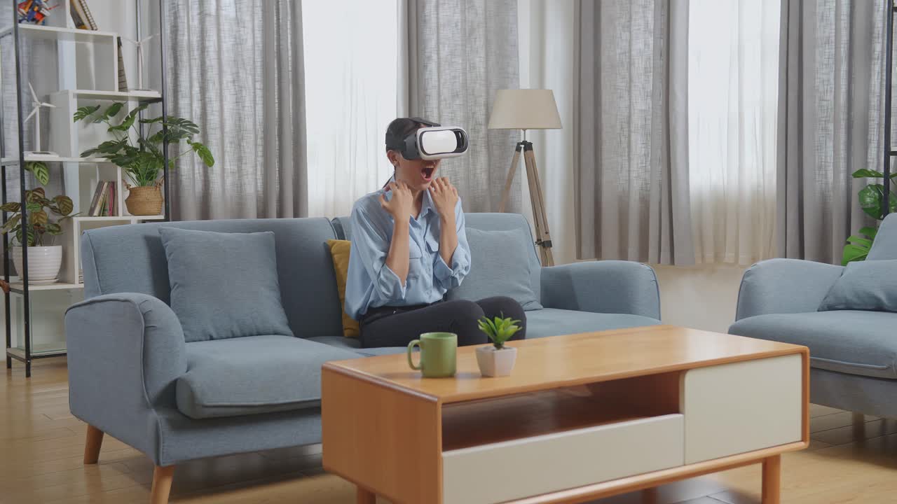 азиатская женщина использует очки виртуальной реальности, сидя на диване в гостиной