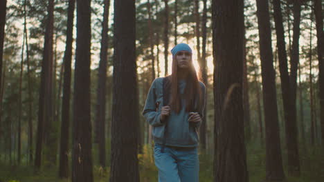 mujer joven con mochila camina a través del bosque tranquilo, bañado en la cálida luz del sol de la noche, mirando contemplativo y conectado con la naturaleza, árboles altos y luz suave