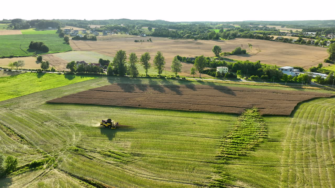 Drohnenaufnahme eines Traktors, der durch lebendige Agrarfelder fährt und unter goldenem Sonnenlicht markante Muster aus grünen und abgeernteten braunen Flächen erzeugt.