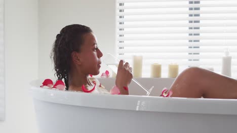 african american woman drinking wine in the bath tub in the bathroom at home