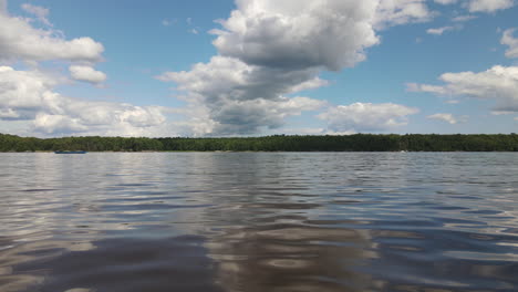 Toma-De-Bajo-Nivel-De-Un-Río,-Que-Muestra-Suaves-Ondulaciones-En-El-Agua,-Nubes-Blancas-Y-Voluminosas.