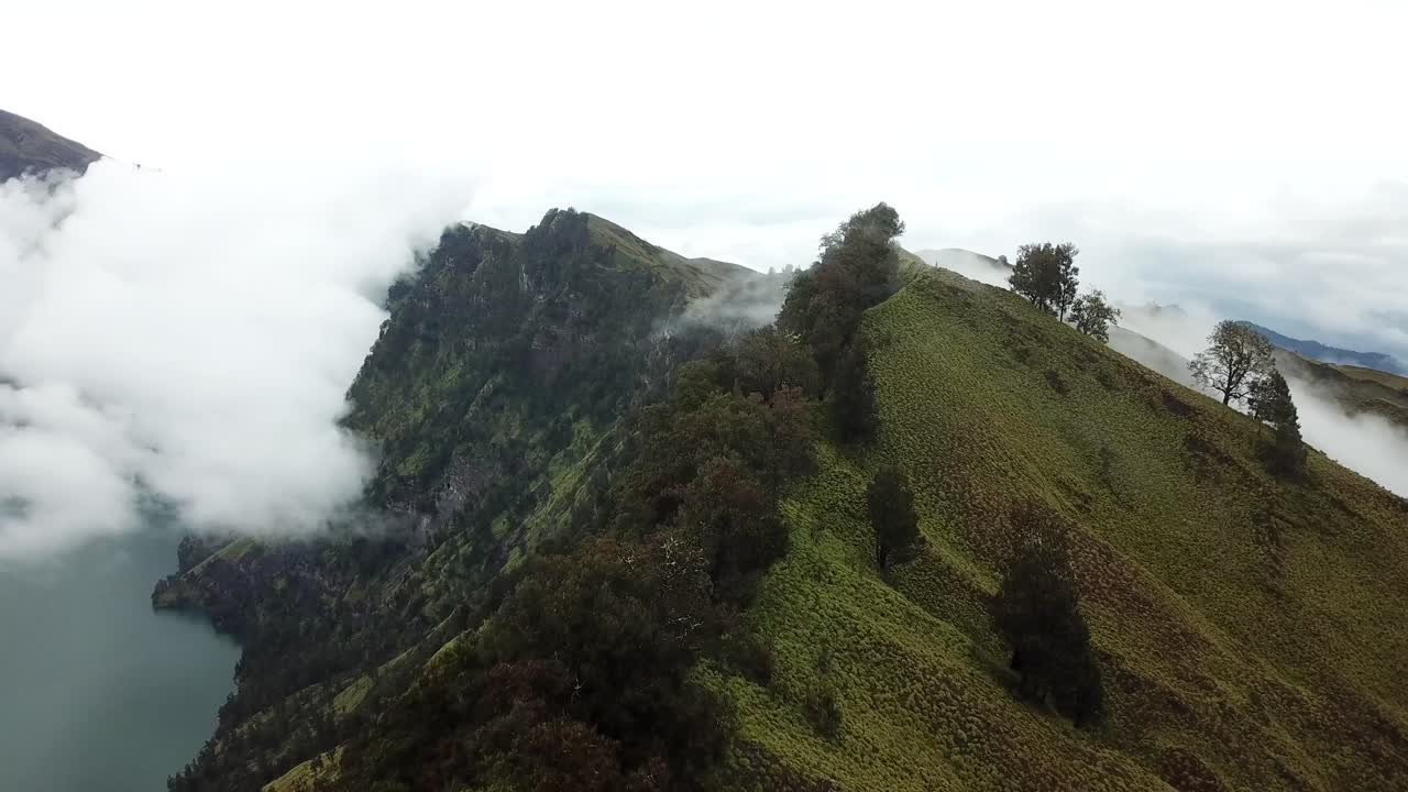 RIPRESA AEREA 4K con panoramica verso il basso del bordo nebbioso del cratere con lago, Vulcano Monte Rinjani, Indonesia.