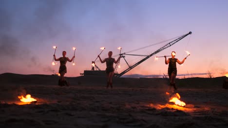 professional artists show a fire show at a summer festival on the sand in slow motion. fourth person acrobats from circus work with fire at night on the beach.