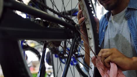 Mechanic-cleaning-bicycle-spoke-in-workshop