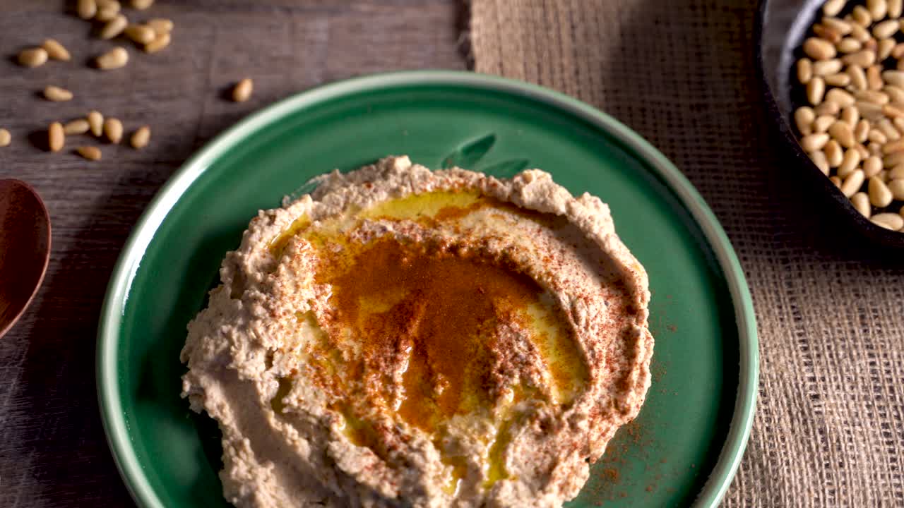 primer plano de ángulo alto deslizándose hacia la derecha de hummus mediterráneo, queso feta, ouzo, aceitunas, piñones y limones