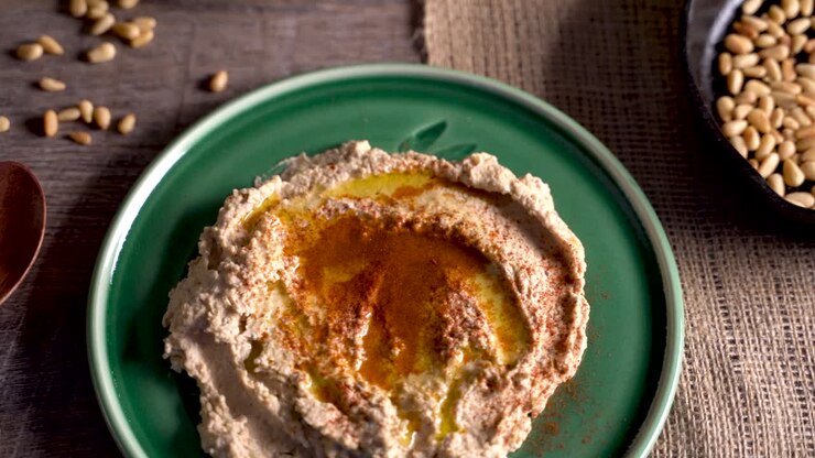 High angle closeup sliding to the right of mediterranean hummus, feta, ouzo, olives, pine nuts and lemons