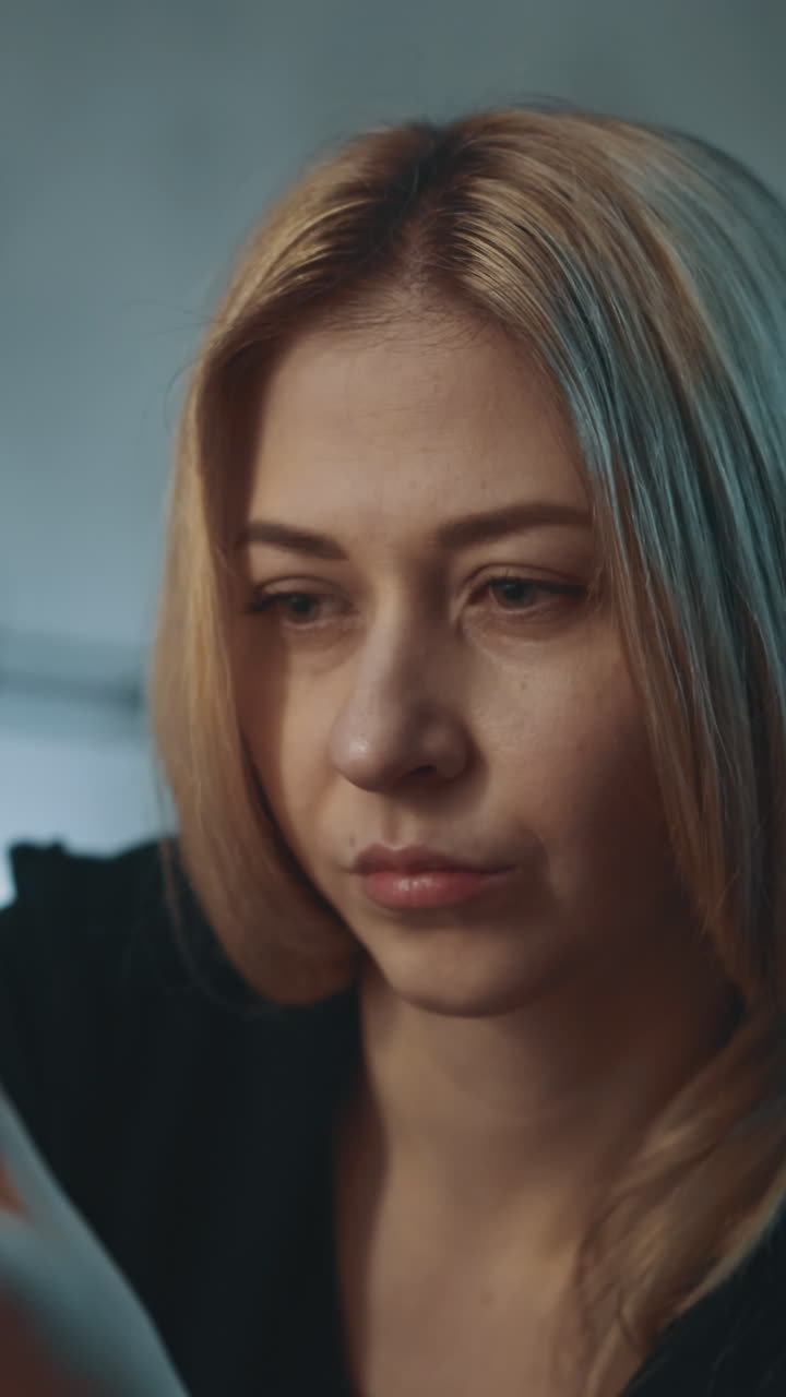 Doubting lady with pill bottle of unregistered nutritional product thinks sitting on blurred background in semi-dark office close view slow motion