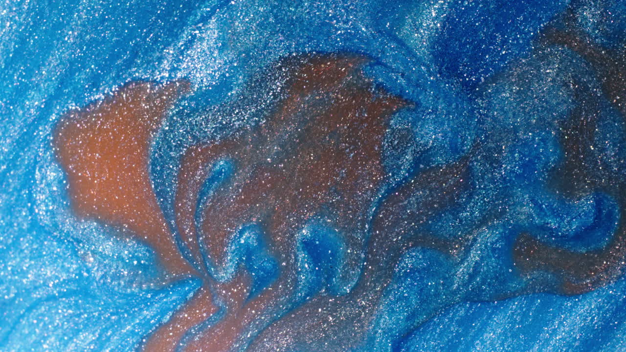 Blue and brown swirling liquid with shimmering glitter particles in a vibrant macro shot
