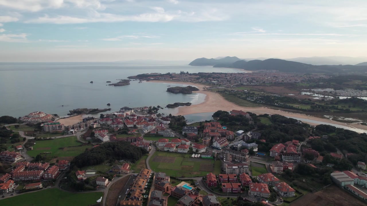 Grande villaggio spagnolo di Suances con molte case dai tetti rossi sulle spiagge di sabbia gialla del tranquillo Golfo di Biscaglia in una giornata estiva. Ripresa panoramica con drone dall'alto