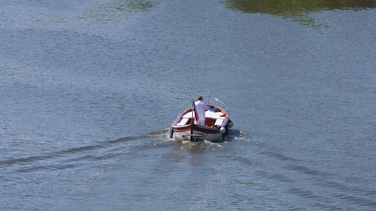 Single small motorboat moves away on calm river, sunny day, steady camera, tranquil atmosphere