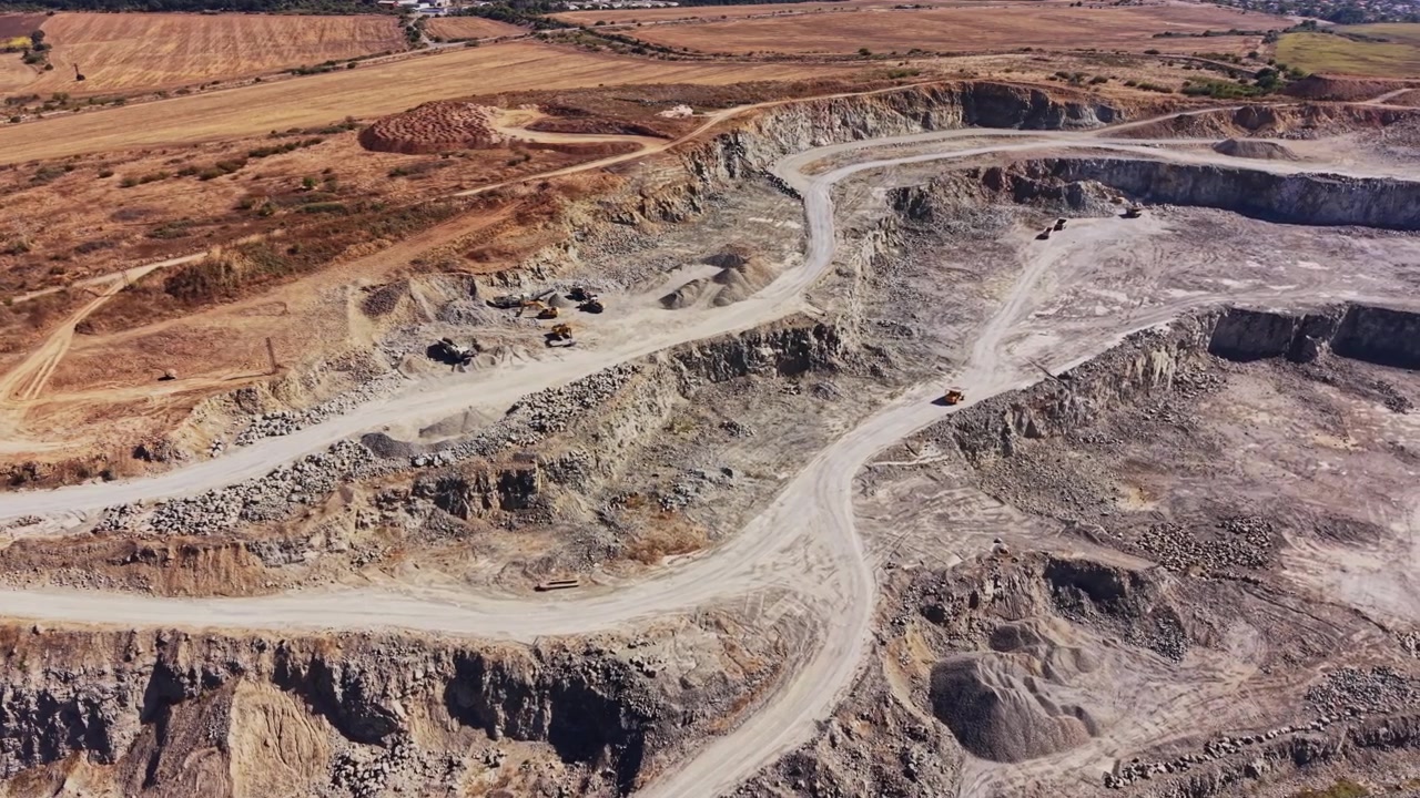 Quarry operation shows large machinery and rocky terrain in a mining site