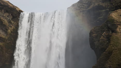 mist from majestic waterfall making a faint rainbow against the backdrop of a cloudy sky