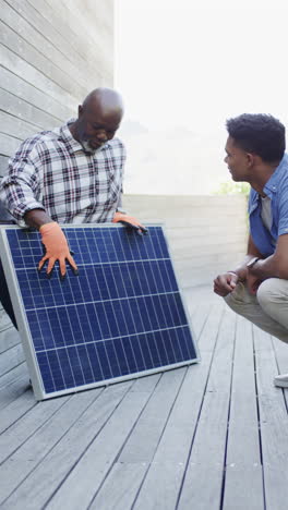 vertical video of african american father explaining solar panel to son outdoors, slow motion