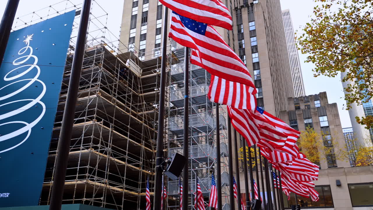 2025年11月8日、アメリカ合衆国ニューヨーク：ロックフェラープラザに立ち並ぶ旗。アメリカの国旗がプラザの上に立ち並び、観光客がロックフェラーセンターを見学しています。