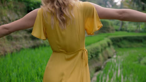 Mujer-Feliz-Caminando-En-Arrozales-Vistiendo-Un-Vestido-Amarillo-Disfrutando-De-Unas-Vacaciones-Explorando-Paisajes-Culturales-Exóticos-Viajando-A-Través-De-Bali-Indonesia