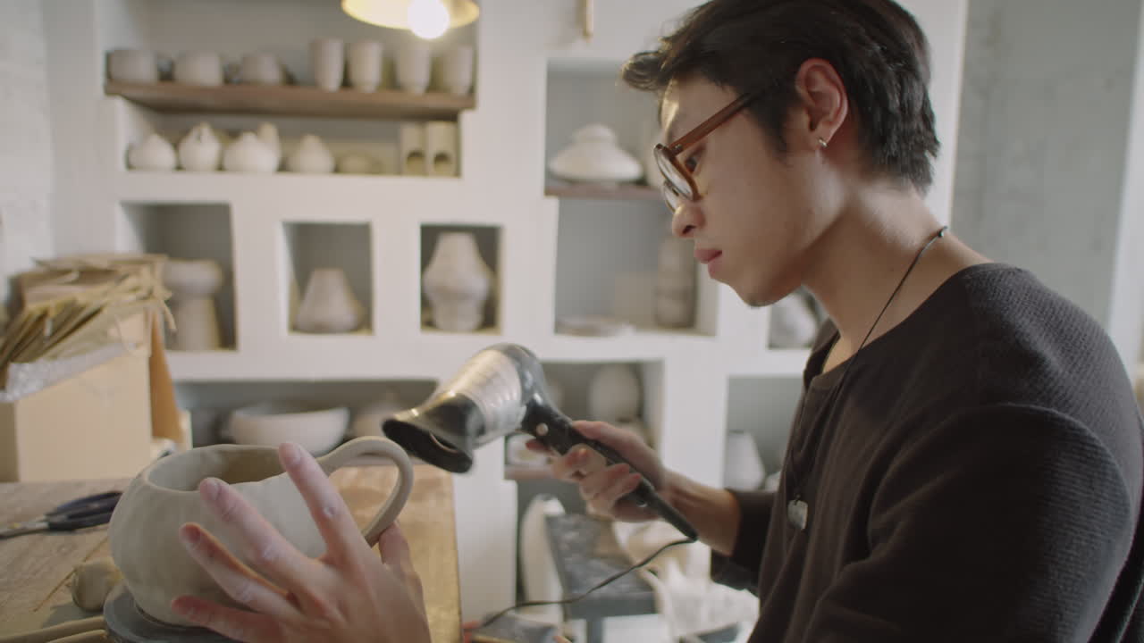 Young Asian Potter Drying Ceramic Mug with Hairdryer