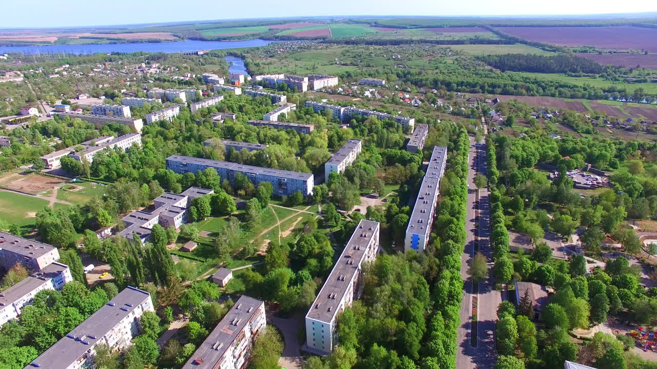 Nice green city panorama lit with bright sun on summer season. Blocks of flats drowning in the greenery. River and farmlands at backdrop.