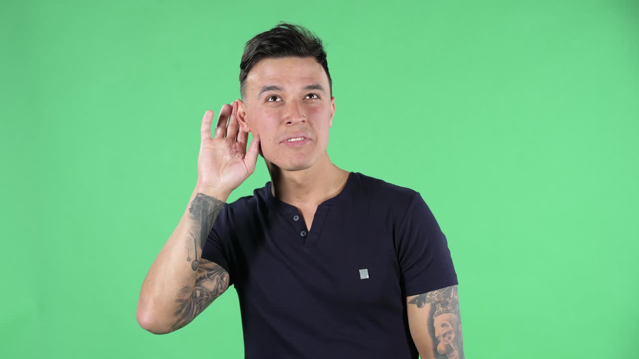 retrato de un joven guapo está sosteniendo la mano cerca de la oreja tratando de escuchar noticias interesantes expresando concepto de comunicación y chismes. pantalla verde