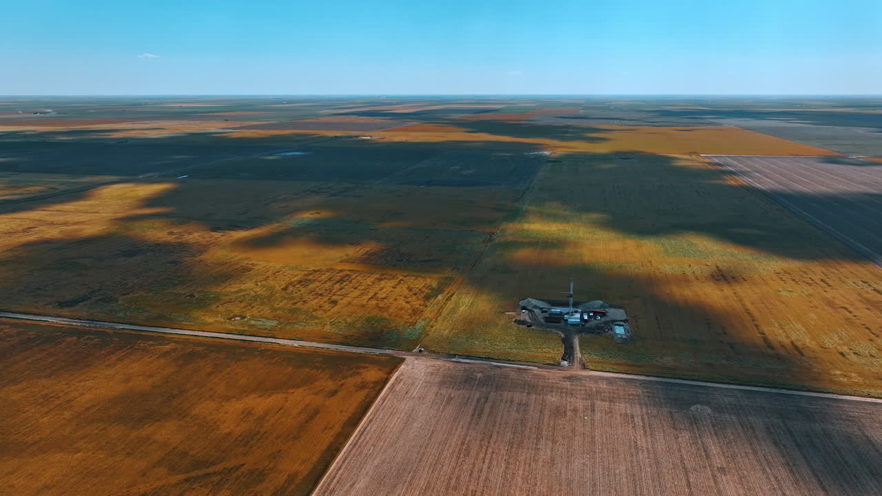 Shadows form clouds fall on the immense field. Drone approaches the little site with oil rig for drilling resources.