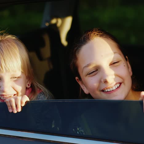 zwei lustige mädchen im alter von 6 und 11 jahren schauen aus dem autofenster