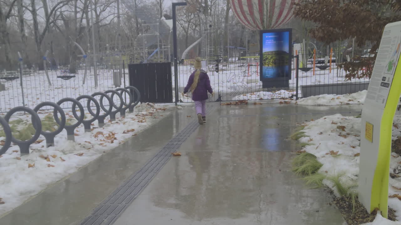 Dynamiske optagelser af et barn, der legende navigerer i en vinterpark og opdager, at legepladsen er lukket, efter at have læst en meddelelse på indgangsporten, hvilket fanger autentisk dagligliv og offentlig sikkerhed