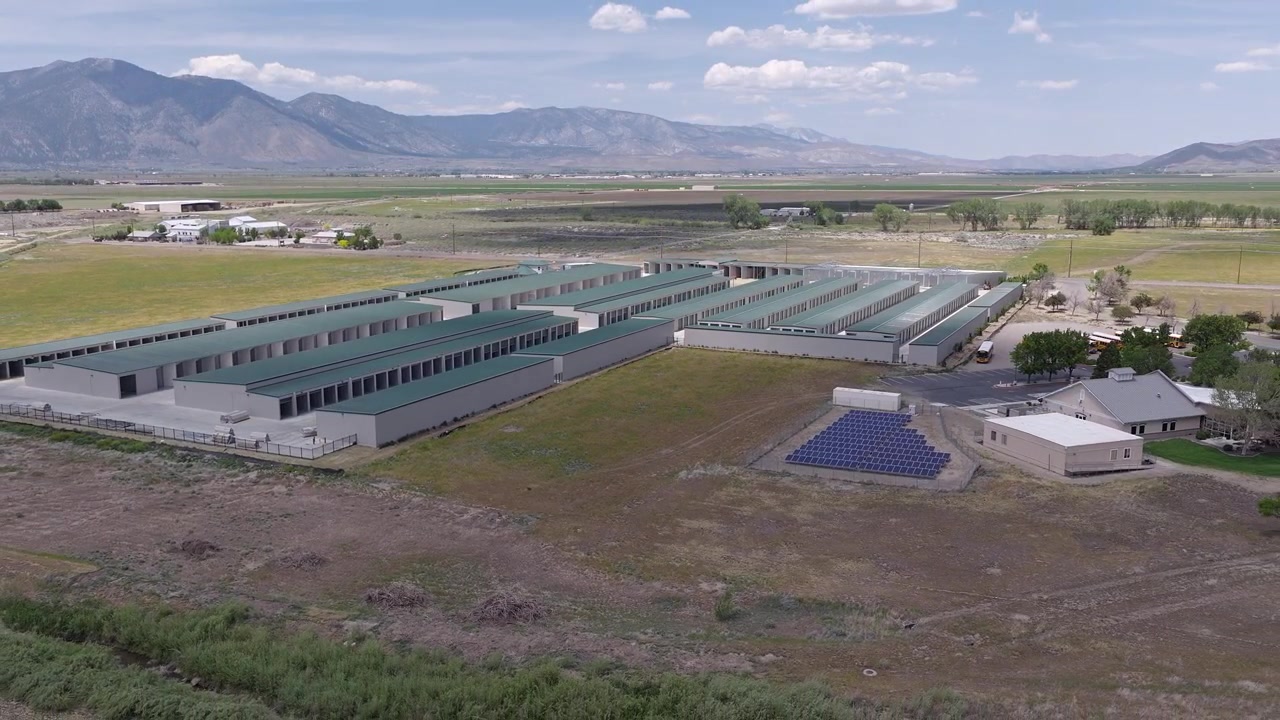 Drone zoom ud-optagelse af et selvopbevaringsanlæg med solpaneler, der leverer vedvarende energi, placeret mod et stort landskab med bjerge i baggrunden i Minden, Nevada.