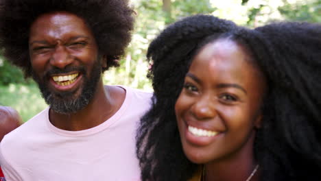 four black adult friends smile to camera in a forest, close up