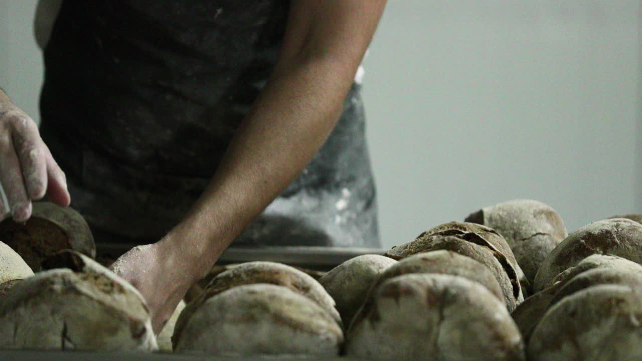 Panettiere che sistema pagnotte di pane a lievitazione naturale appena sfornate sulla rastrelliera - rallentatore.