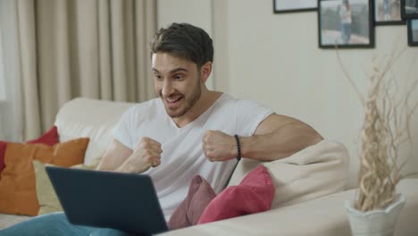 hombre feliz celebrando el éxito con una computadora portátil en el sofá en casa