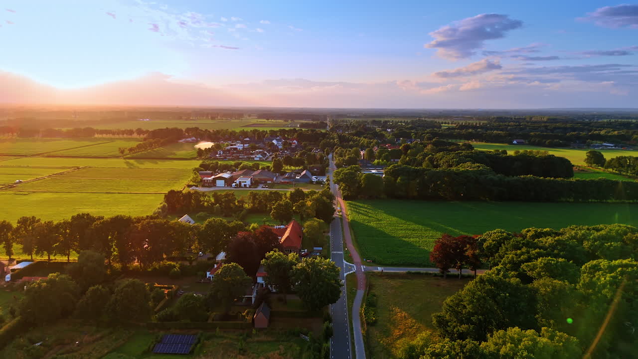 Sunset over green fields. Vibrant green fields stretch under a colorful sunset, while roads weave through small clusters of houses and trees