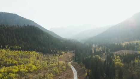 Beautiful-road-through-mountain-range-valley-forest-during-fall,-aerial-view