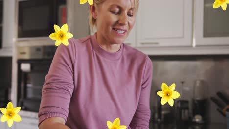 Animation-of-flowers-over-caucasian-woman-peeling-melon-in-kitchen